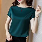 A woman wears a short-sleeved, solid dark green satin blouse with a simple boat neckline.