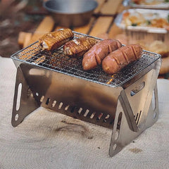 A portable stainless steel folding camping grill with two chicken wings and two sausages cooking.