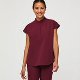 A woman wears a burgundy medical scrub top with a mandarin collar and matching scrub pants.