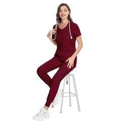 A woman wearing a maroon V-neck scrub top and matching jogger pants with a stethoscope.