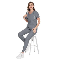 A woman wearing a grey scrub set with a stethoscope around her neck while sitting on a stool.