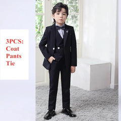 A young boy wears a formal black three-piece suit with a patterned bow tie and dress shoes.