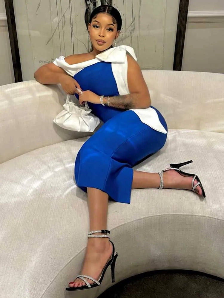 A woman wears a blue mid-length dress with a white bow detail on the shoulder.