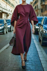 A woman wears an elegant, ankle-length burgundy dress with bat sleeves and a fitted waist.