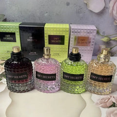 Four OMY Secrets perfume bottles with textured glass and matching boxes are arranged in a row.