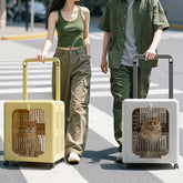Two people walk across a crosswalk pulling portable, wheeled pet carriers containing cats.