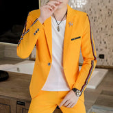 A man wears a bright yellow slim-fit suit with black and white striped sleeve detailing.