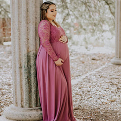 A pregnant woman wears a long-sleeved, V-neck mauve maternity gown with a lace bodice.
