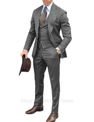 A man wears a grey three-piece suit with a peak lapel, white shirt, and brown tie.