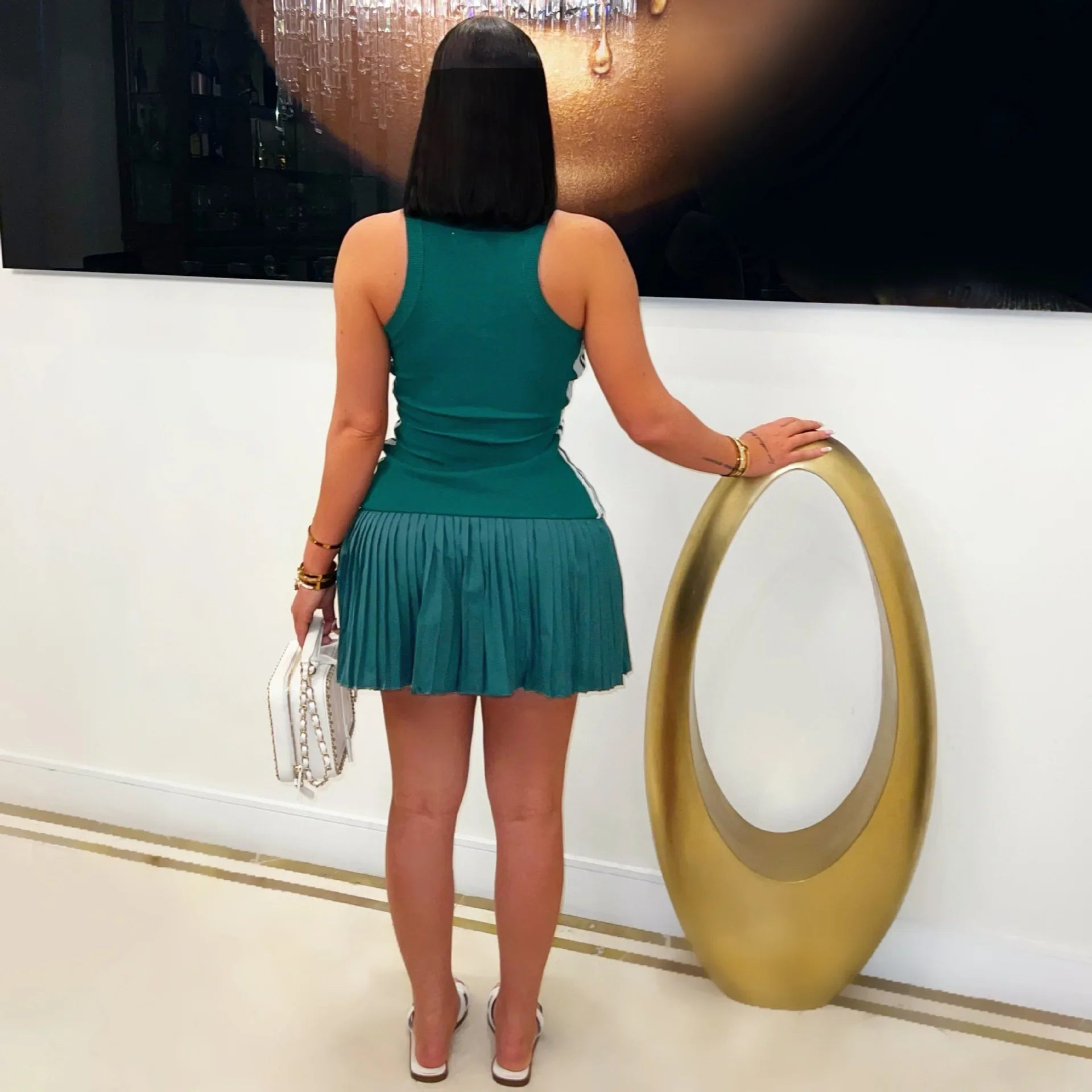 A woman wears a sleeveless green mini dress with a pleated skirt and a sporty racerback design.