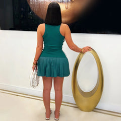 A woman wears a sleeveless green mini dress with a pleated skirt and a sporty racerback design.