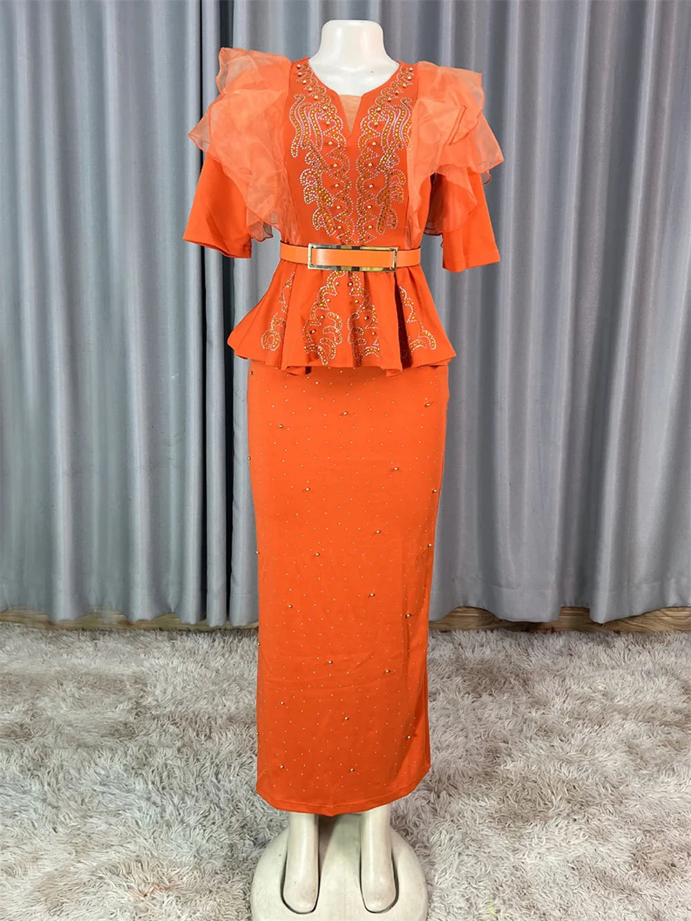 An orange ankle-length dress with a peplum waist, rhinestone embellishments, and ruffled sleeves.