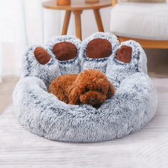 A fluffy, grey, bear paw-shaped pet bed with a small brown dog resting inside.