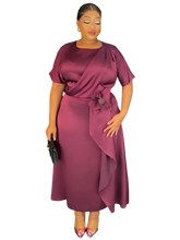 A woman wears a plum-colored midi dress with short sleeves, a draped bodice, and a floral accent.