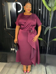 A woman wears a plum-colored midi dress with short sleeves, a draped bodice, and a floral accent.
