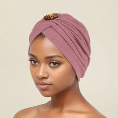 A woman wears a dusty pink pleated turban featuring a decorative diamond-style brooch.