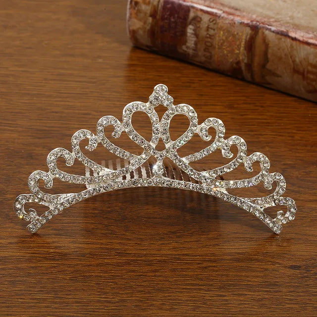 A silver rhinestone tiara with a comb attachment sits on a wooden surface.