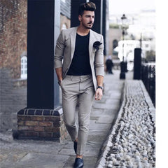 A man wears a beige two-piece suit with a black t-shirt and dark loafers.