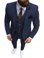 A man wears a navy blue three-piece slim-fit suit with a brown tie and white sneakers.
