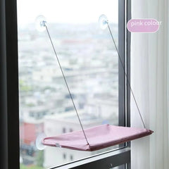 A pink cat hammock suspended by suction cups on a glass window.