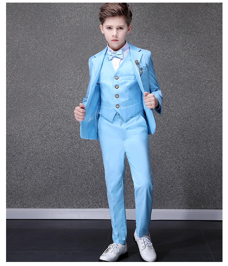 A boy wears a sky blue formal suit with a matching vest, bow tie, and white dress shoes.