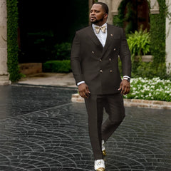 A man wears a dark brown double-breasted suit with a white shirt and a gold bow tie.
