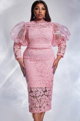 A woman wears a pink lace midi dress with sheer puff sleeves and a high neckline.