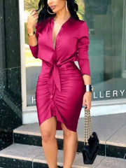 A woman wears a long-sleeved, deep V-neck magenta bodycon dress with a front tie detail.