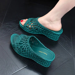 A pair of dark green wedge slippers with a hollow-out rope design and a peep toe.