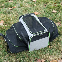A grey and black expandable pet carrier with mesh panels sitting on grass.