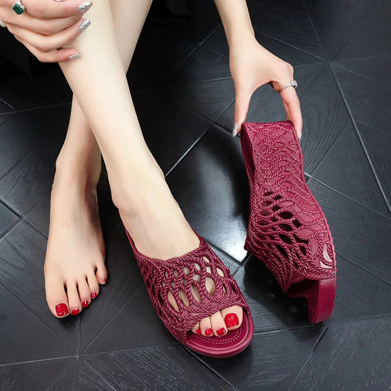 A pair of burgundy wedge slippers featuring a hollow-out woven design and a peep-toe style.