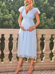 A pregnant woman wears a light blue V-neck maternity dress with flutter sleeves and mesh overlay.