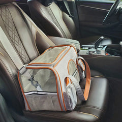 A grey and orange soft-sided pet carrier sits on the leather passenger seat of a car.