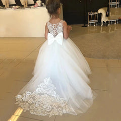 A young girl wears a white sleeveless tulle flower girl dress with lace appliques and a back bow.