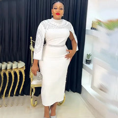 A woman wears a white midi-length dress with silver beaded embellishments on the cape and waist.