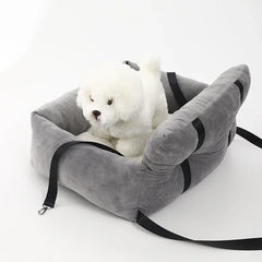 A plush grey pet car seat with black safety straps and a small white toy dog sitting inside.
