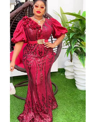 A woman wears a long, burgundy sequined evening gown with puff sleeves and a gold-buckled belt.