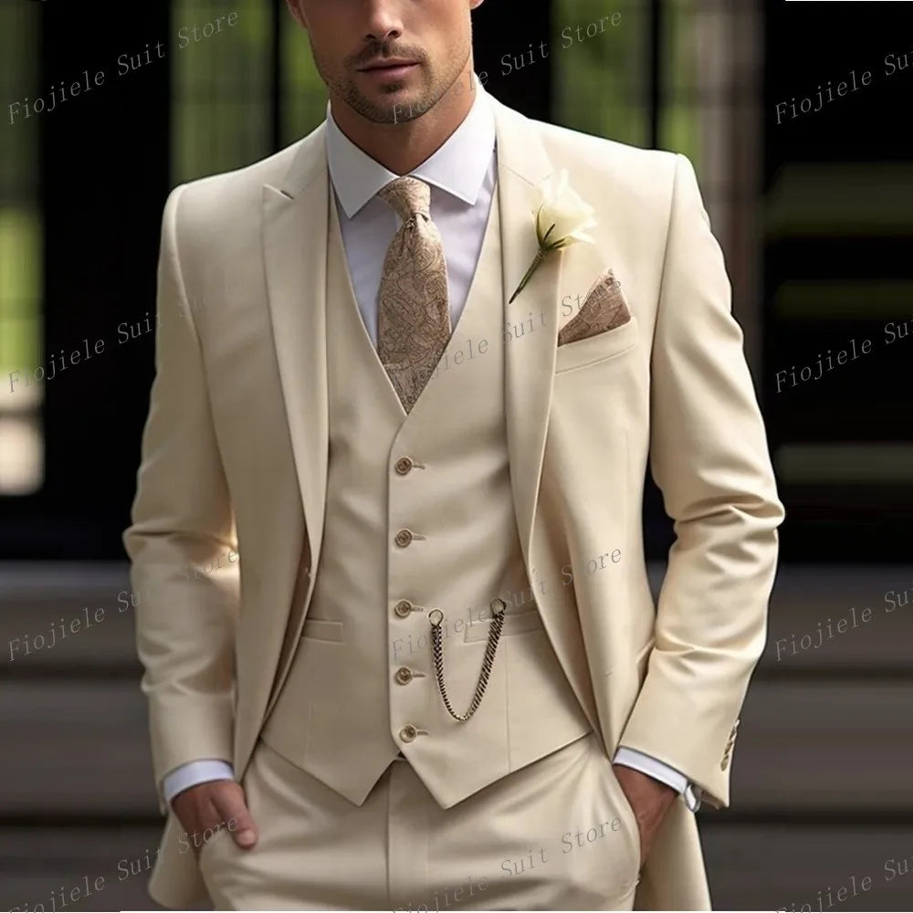 A man wears a beige three-piece suit with a patterned tie, a pocket square, and a pocket watch chain.