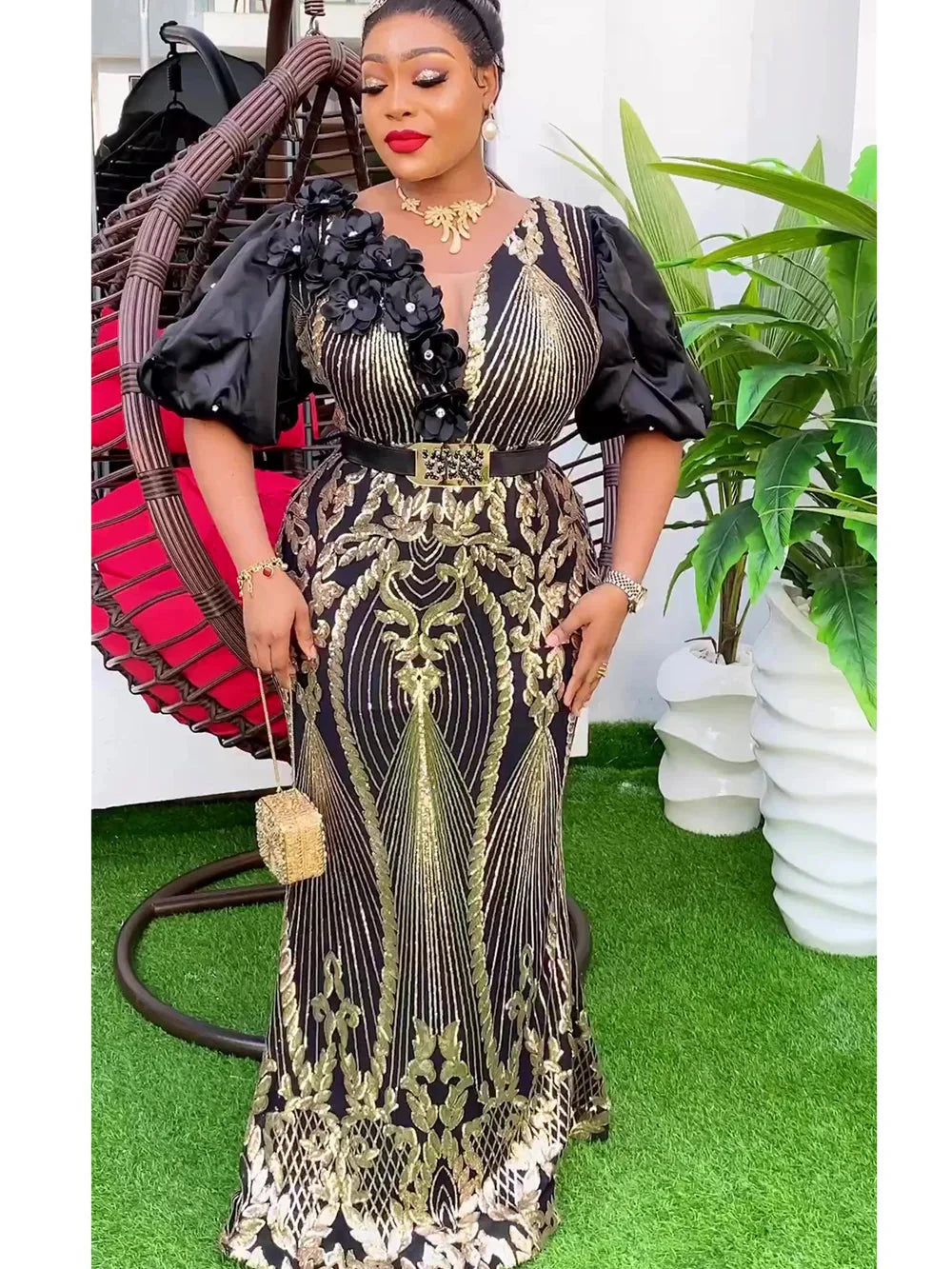 A woman wears a black and gold sequined floor-length evening gown with puff sleeves and a belt.