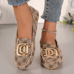 A pair of beige patterned fabric loafers featuring a gold D-shaped metal ornament on the front.