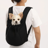 A person wears a black mesh pet backpack with a small white dog peeking out from the top.