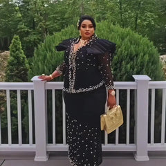 A woman wears a black two-piece suit with pearl embellishments and ruffled shoulders.