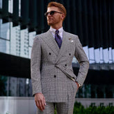 A man wears a double-breasted, glen plaid suit with peak lapels and a patterned tie.