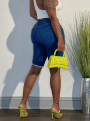A woman wears slim-fit, knee-length deep blue denim Bermuda shorts with a frayed hem.
