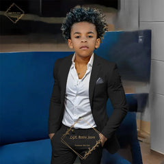 A young boy wearing a black single-breasted suit jacket and matching trousers with a white shirt.