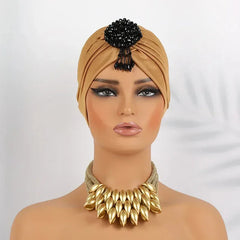 A tan pleated turban headscarf featuring a black beaded embellishment on the front.