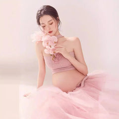 A pregnant woman wears a pink strapless tube top and a long mesh tutu skirt for a photo shoot.