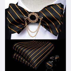 A black and gold striped bow tie set featuring a decorative brooch, pocket square, and cufflinks.