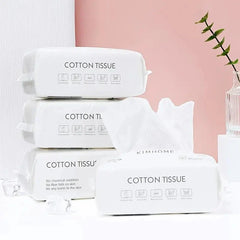 A stack of white rectangular disposable cotton face towel packs with a single sheet pulled out.