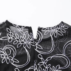 A close-up of the black mesh neckline featuring white floral embroidery and a back zipper.